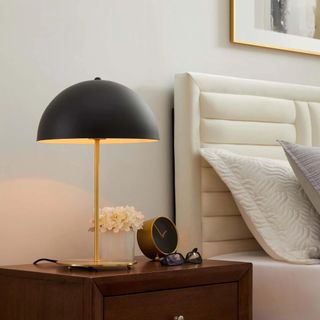 A mid-century modern gold and black table lamp on a nightstand