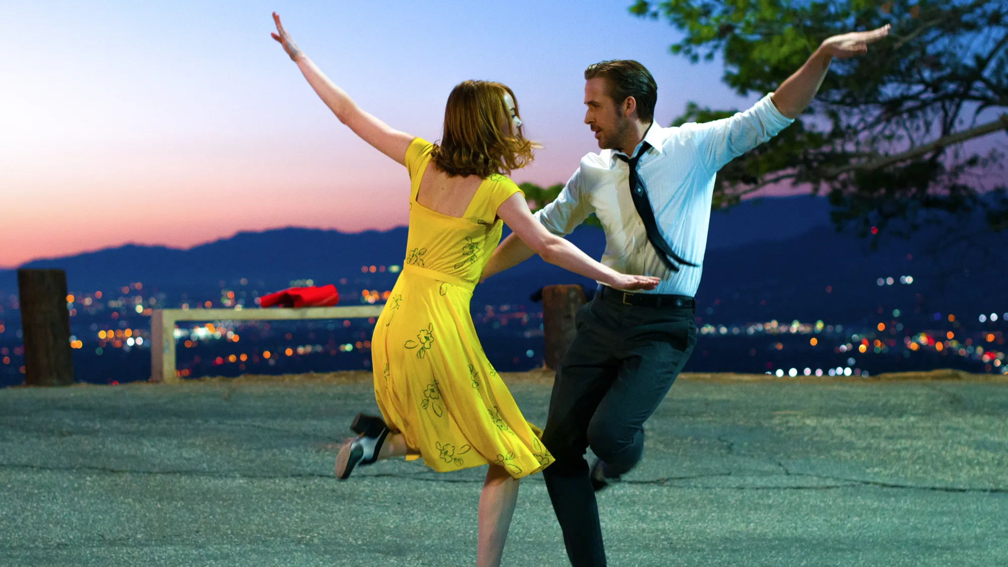 La La Land still. Mia and Sebastian dance towards each other with one arm outstretched, with the LA skyline behind them.
