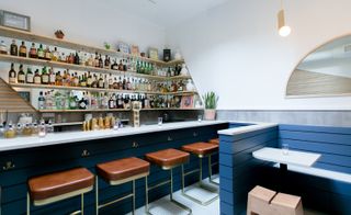 A view along the bar with blue wood panelling and mirrored shelving for bottles of spirits