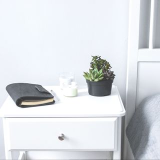 Tiny succulents, candles and black notebook on bedside table in the bedroom in scandinavian style home. Scandinavian interior in gray and white colors - stock photo