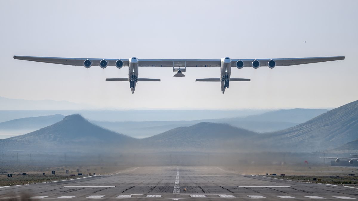 A dual-fuselage aircraft lifts off carrying a test vehicle