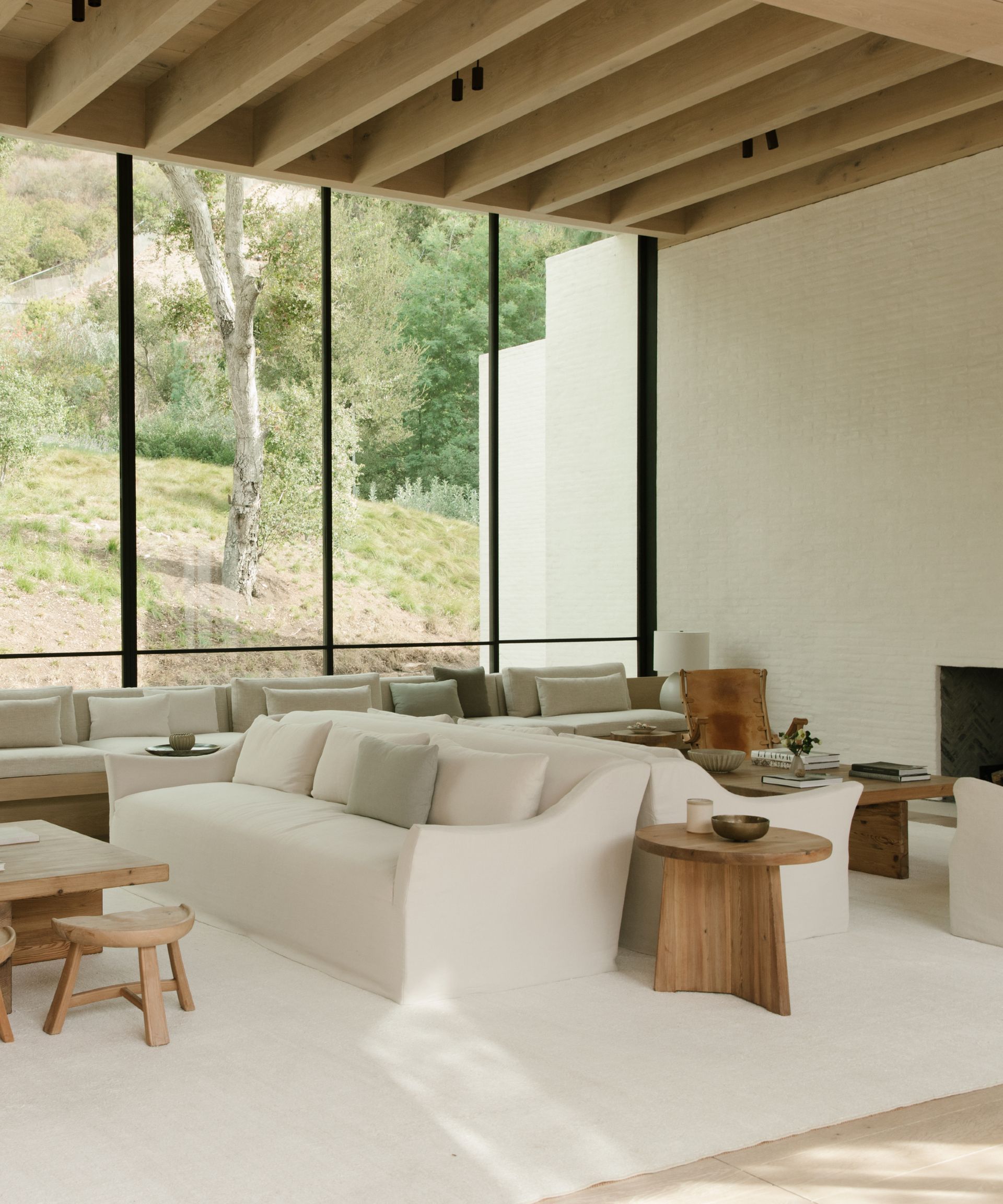 make your home feel like a sanctuary, white and wood scheme with multiple seating, back to back couches, low slung stools, coffee tables, large windows with view outside, beams