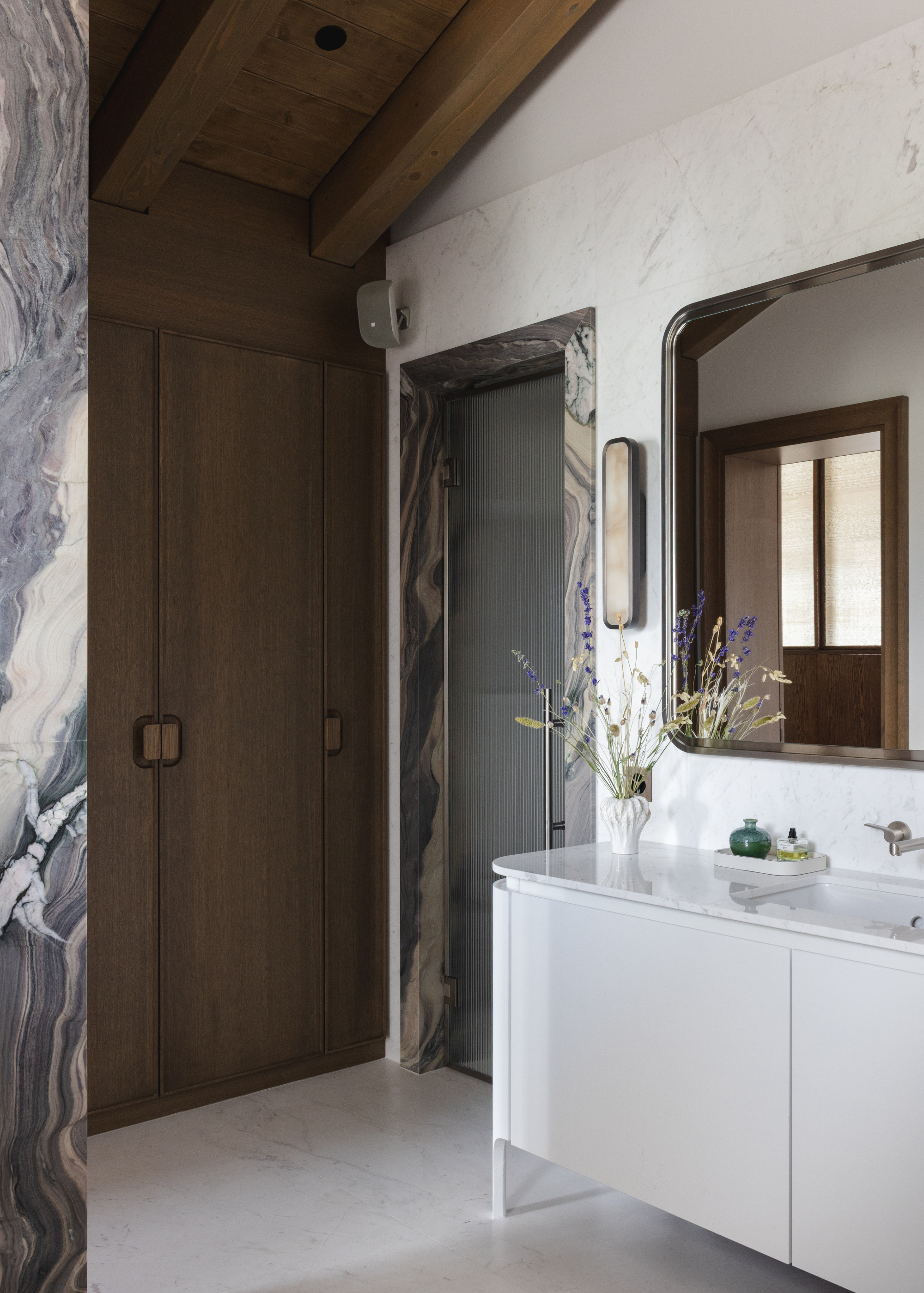 chalet bathroom with grey marble architraves over the doors, wooden ceilings, and white marble floors