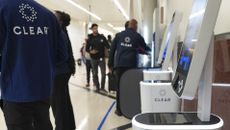 Clear employees stand near Clear kiosks, helping travelers enroll in the program at the airport.