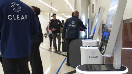 Clear employees stand near Clear kiosks, helping travelers enroll in the program at the airport.