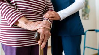 lower body shot of a nurse helping an elderly woman with a walking stick