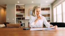 A woman works on retirement planning paperwork at her dining room table.