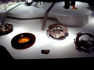Four circular ornaments are the focal point of the photo. Left to right: A multi-coloured bowl; a black rim bowl with an orange centre; two circular bowls with holes in.