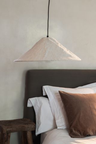 A close up of a bed with neutral colors and an oversized pendant lamp shade