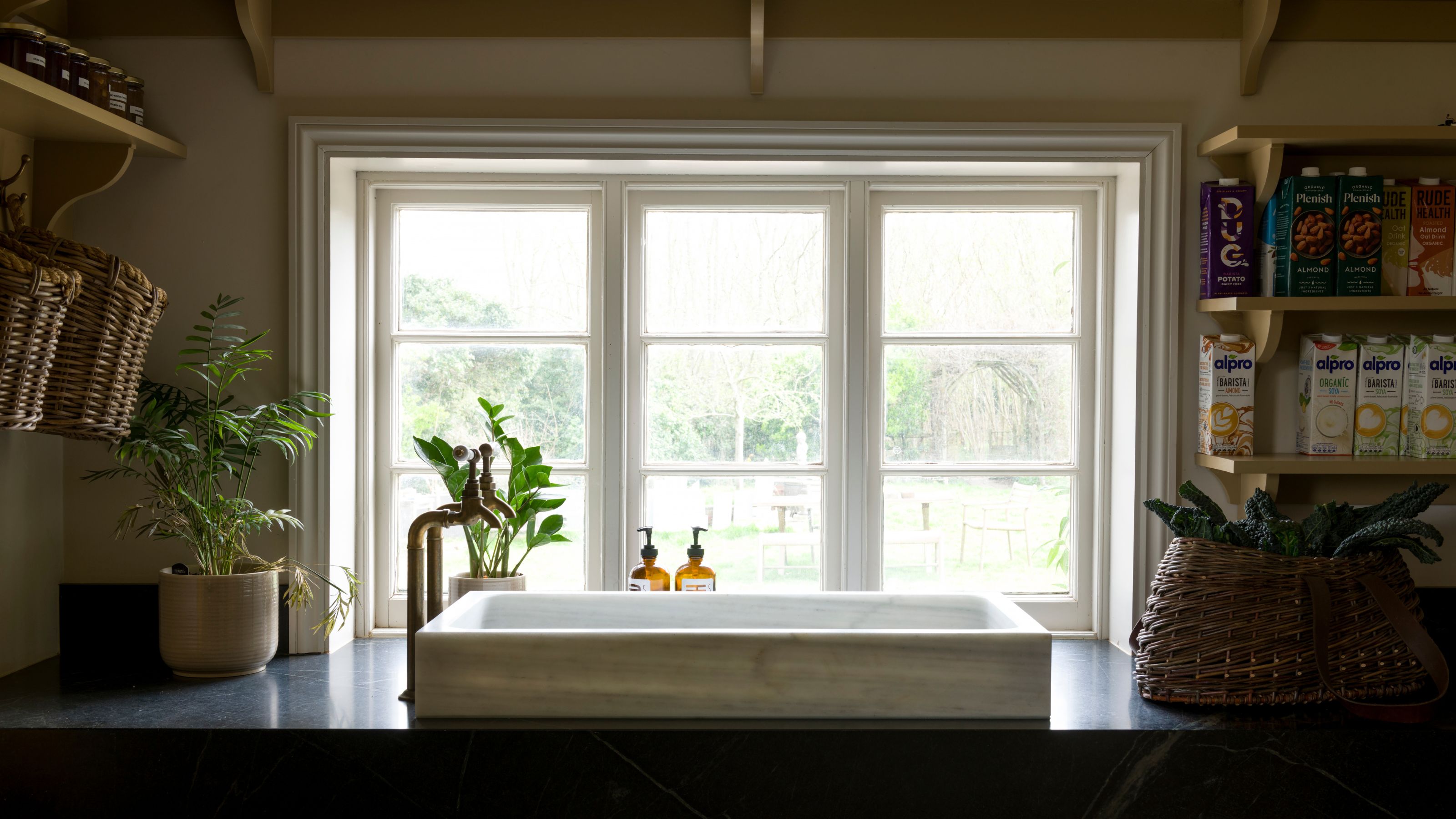 A large marble kitchen sink in front of a large window with open shelving on either side of the walls 