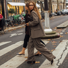 A quest attends Paris fashion week spring/summer 2025 wearing brown suit set and glasses carrying clutch bag