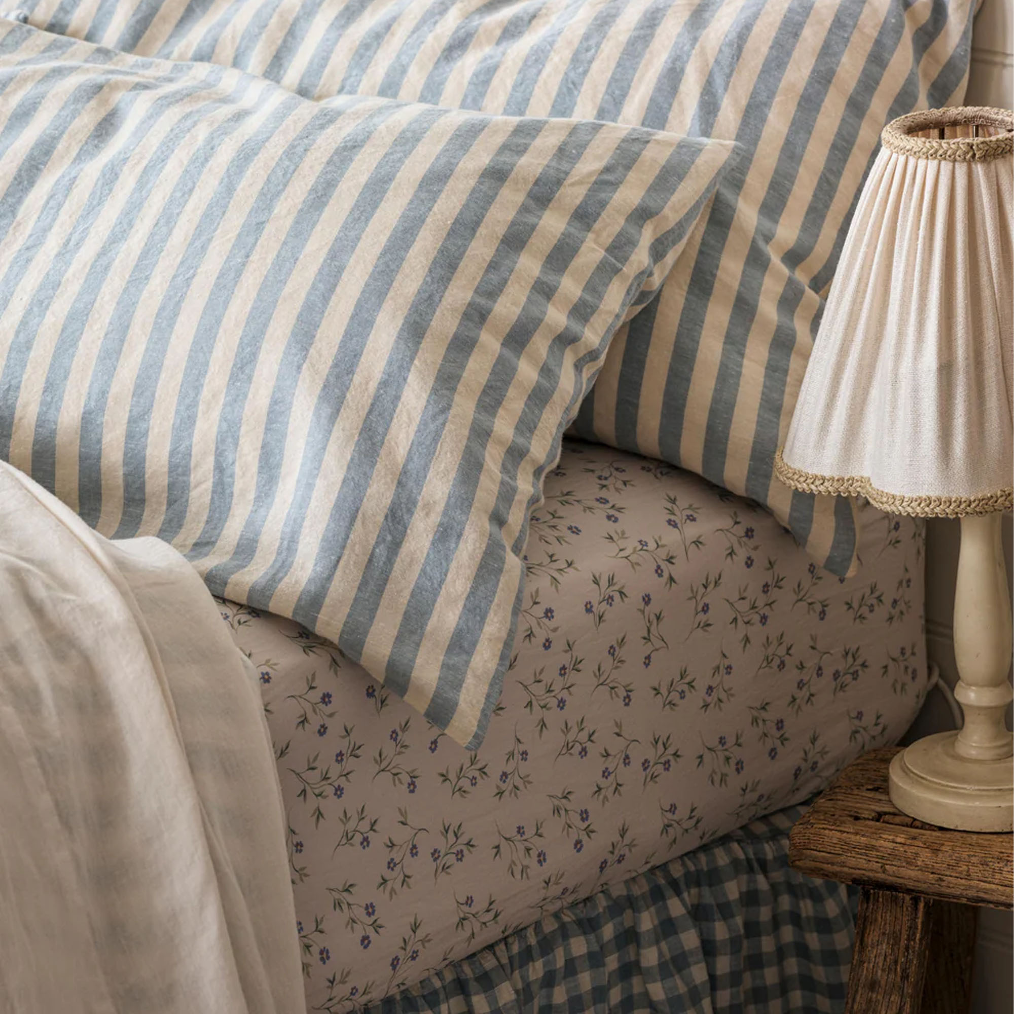 Piglet in Bed Coastal Blue Pembroke Stripe 100% Linen Pillowcase on a bed with a ditsy floral fitted sheet