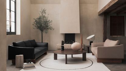 A neutral living room with lime wash walls, a dark fabric sofa, and a single arm chair