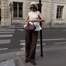 maryljean wears a striped trouser outfit in summer 2026. She wears brown pin-striped trousers with loafers, a peplum top, and a crochet headscarf. She finished with a Ganni bag and large silver hoops.