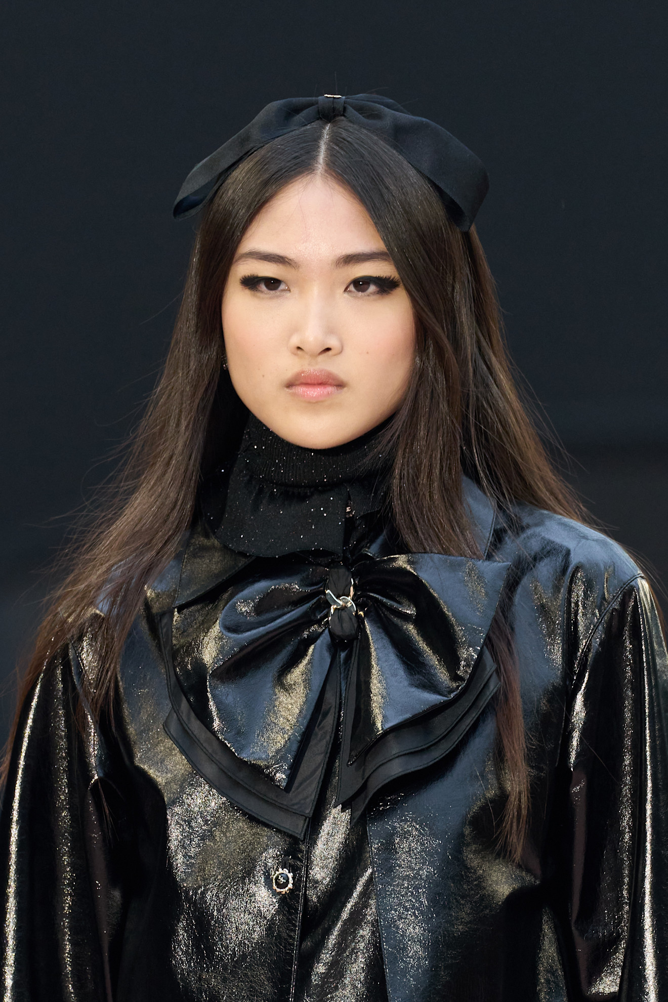 model with long dark hair wearing a large satin hair bow accessory on top of her head