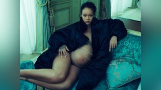 A pregnant Rihanna sits on a turquoise velvet chaise lounge, draped in a black fur coat with a silver chain draped across her bare stomach.
