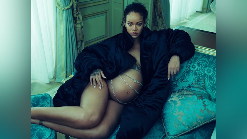 A pregnant Rihanna sits on a turquoise velvet chaise lounge, draped in a black fur coat with a silver chain draped across her bare stomach.