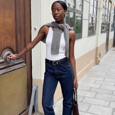 Woman in white tank top, sweater and dark wash jeans