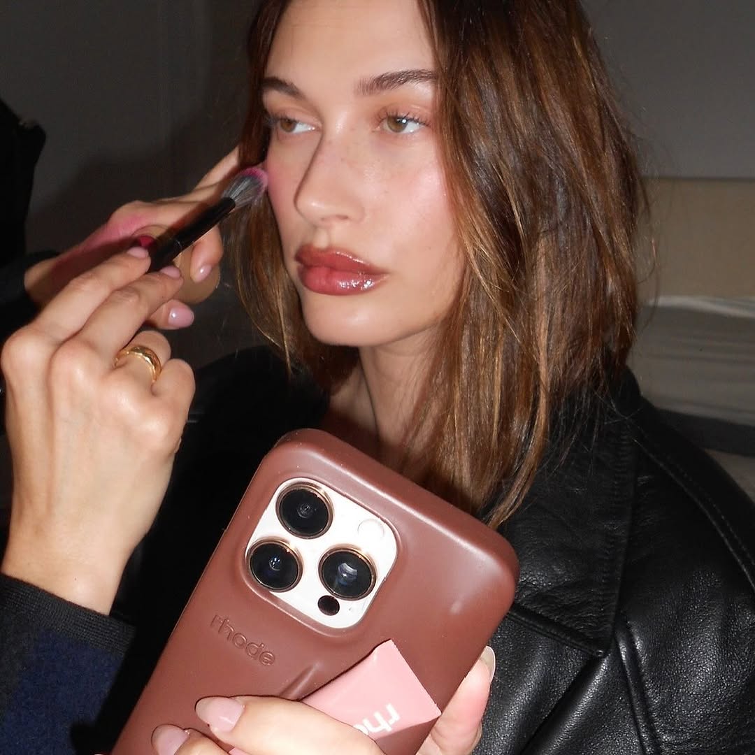 A photo of a makeup artist diffusing a berry pink blush shade over Bieber's cheeks.