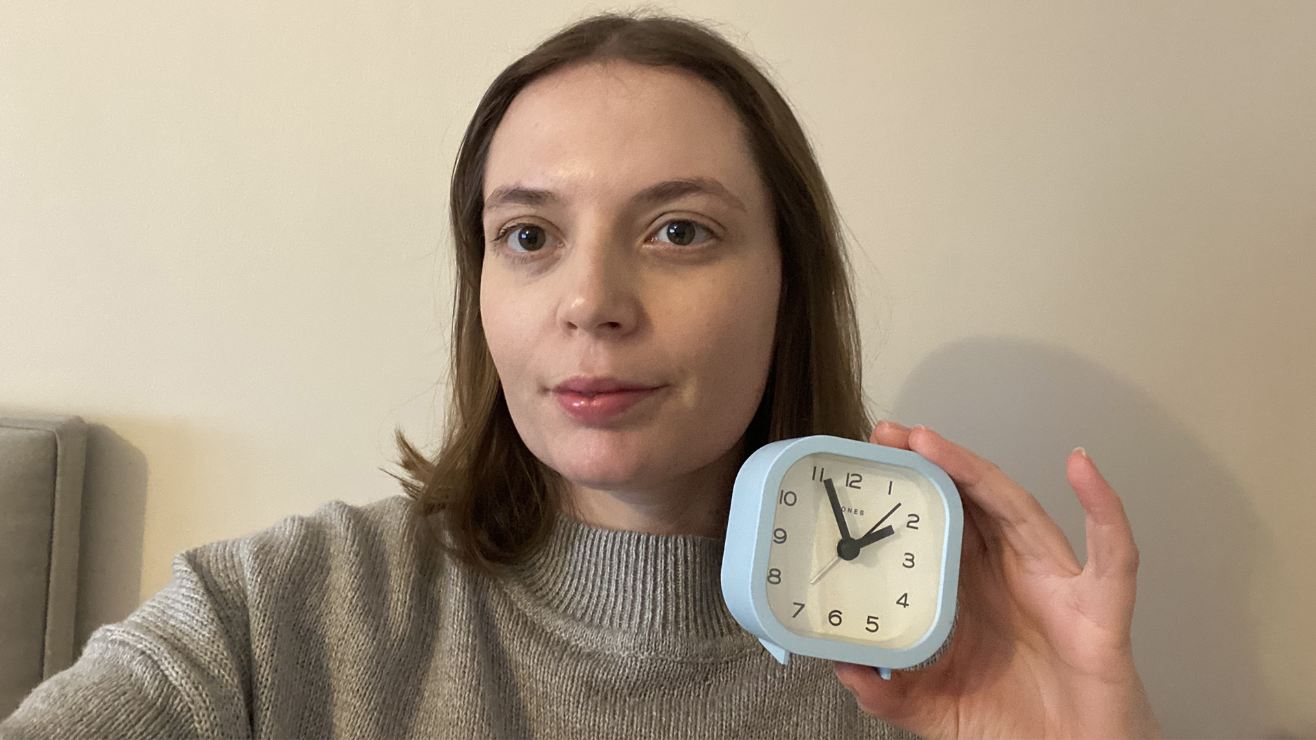 An image of sleep writer Ruth Jones holding a small alarm clock in front of a beige wall