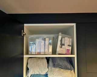 Matte navy floor to ceiling closet open and the top shelf has two boxes with medicines