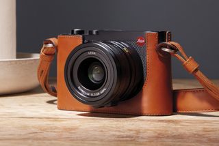 Leica Q3 in a brown leather case and on a wooden table