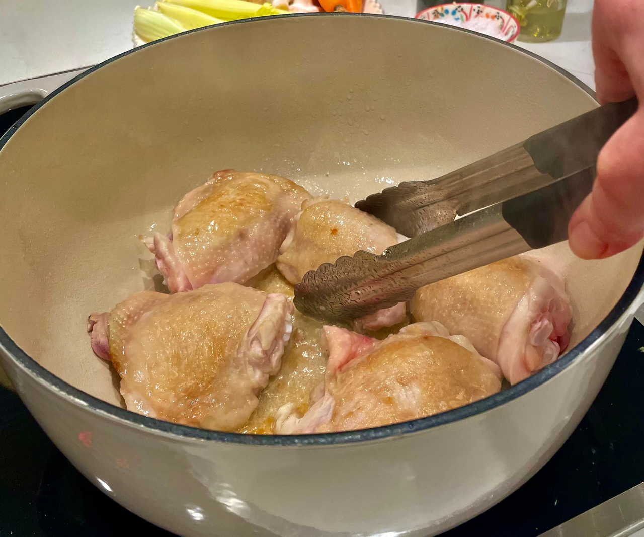 Sizzling chicken thighs in the Lodge 6QT Enameled Cast Iron Dutch Oven, turning them with tongs.