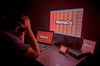 Somebody sitting at their desk in front of various devices that have been locked by WannaCry