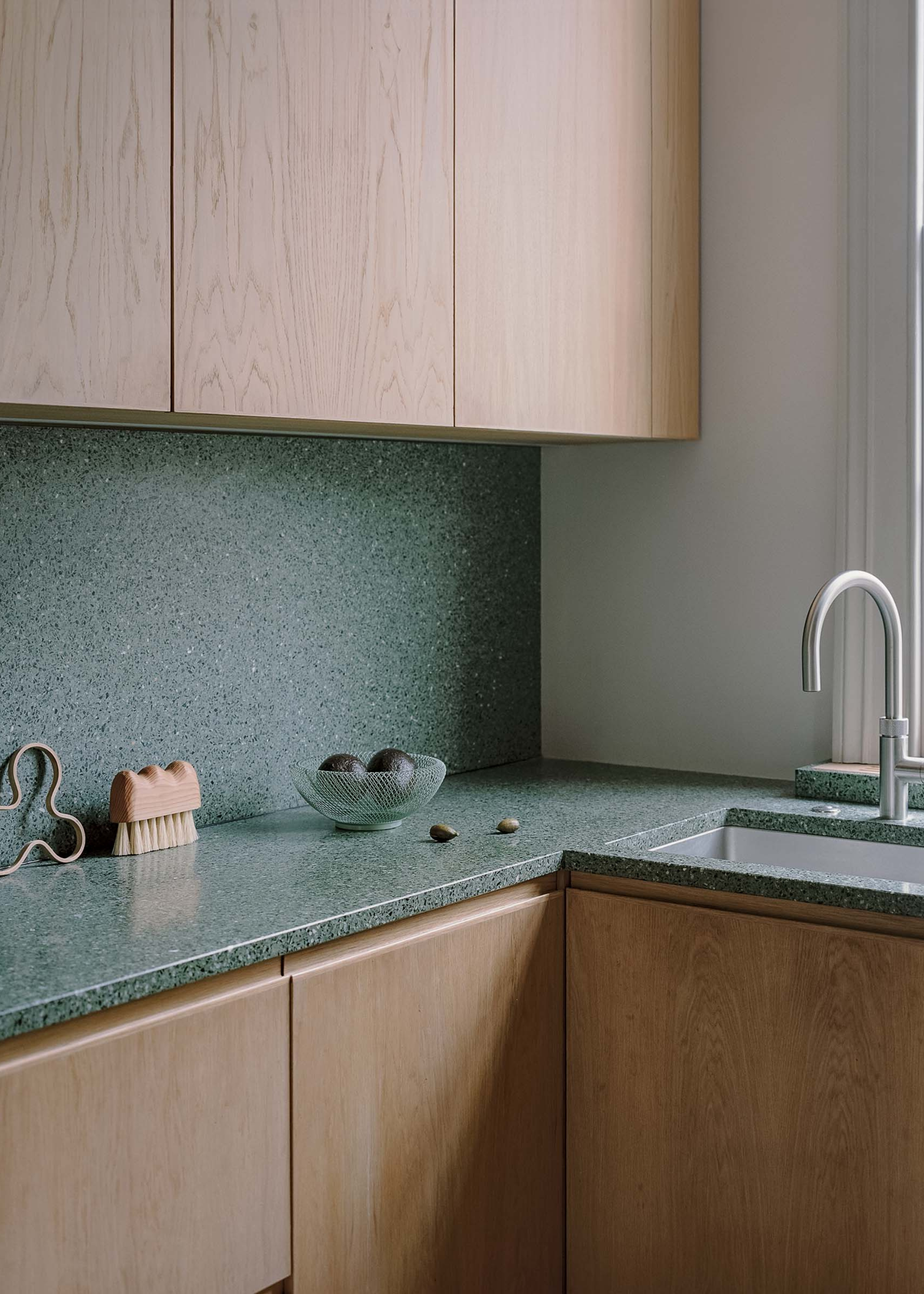 corner of a small kitchen with seamless light oak cabinetry and dark green terrazzo counters and backsplash