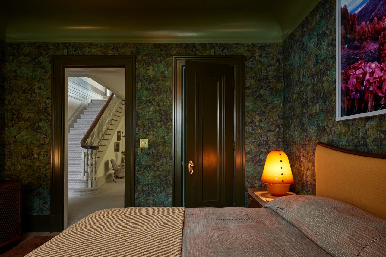 A green color drenched bedroom with botanical wallpaper, a green ceiling , dark green woodwork and a dressed bed