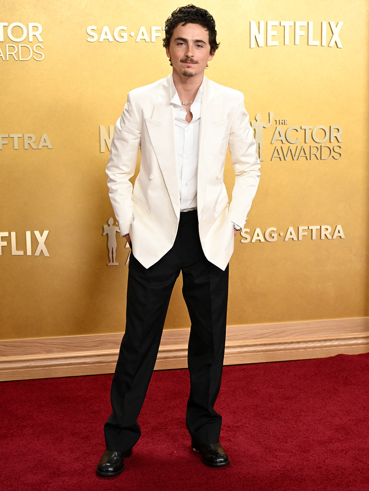 Timothee wears a white suit, white shirt, and black pants.