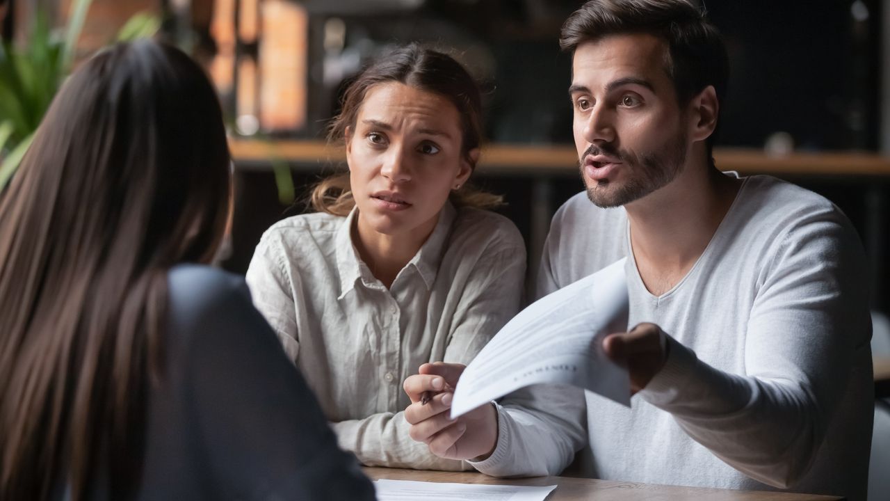 A couple look very unhappy with the woman helping them at a desk in an office.