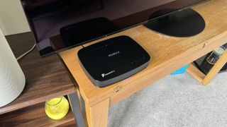 Humax Aura smart PVR viewed at an angle on wooden unit in front of a TV