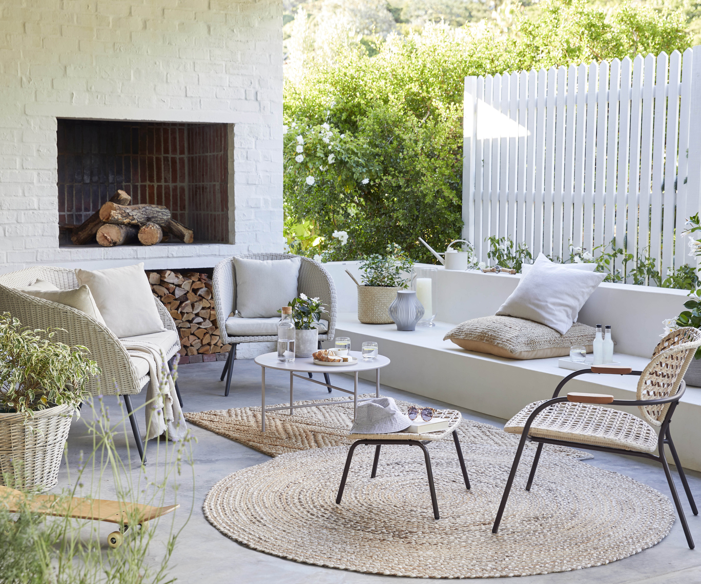 white painted picket fence behind patio with seating and built in fireplace in wall