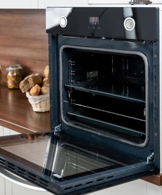 An image of a black oven with its door open in a kitchen with wooden countertops and white cabinets