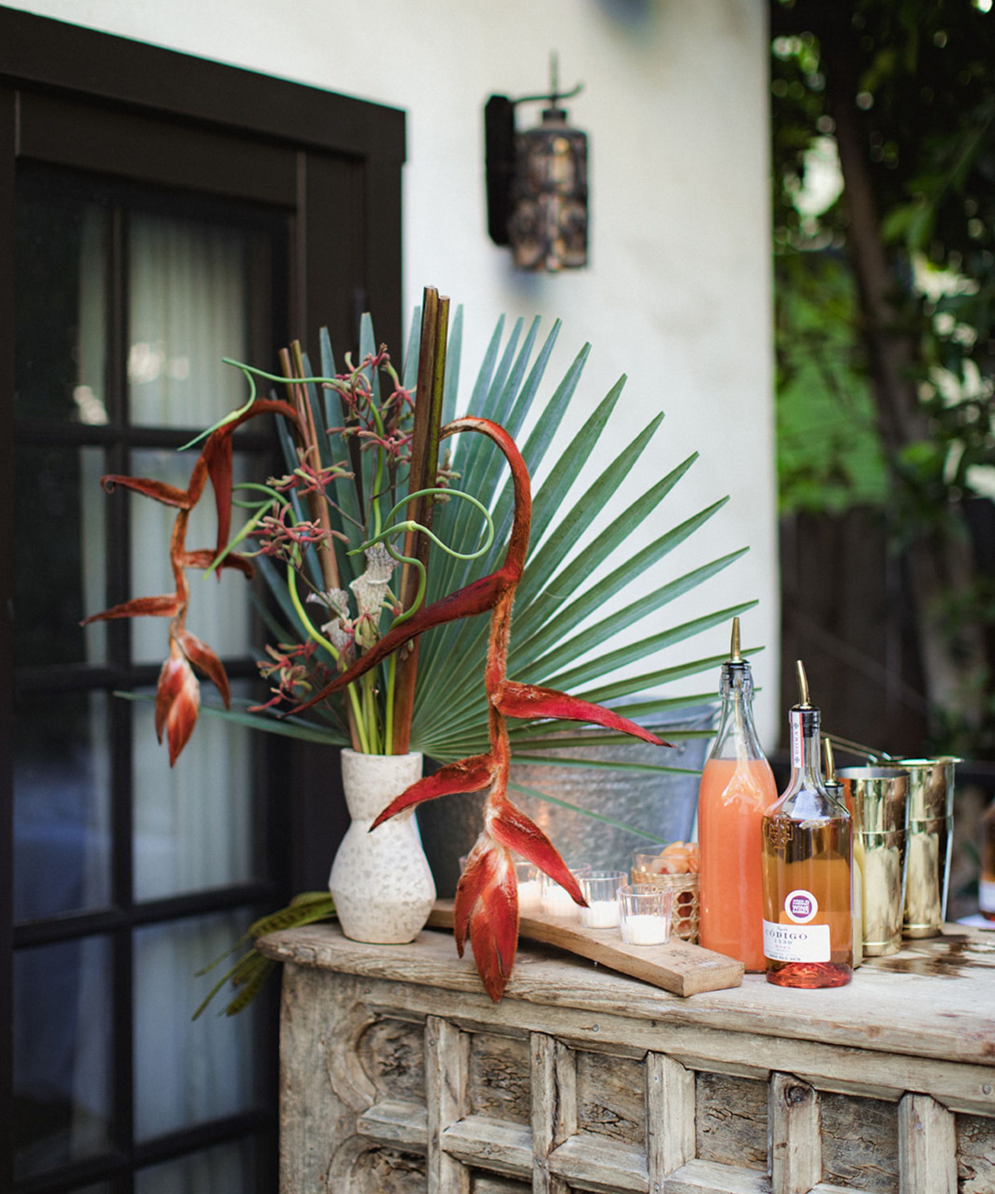 Rustic outdoor bar with bottles and cockail shakers and a tropical plant display