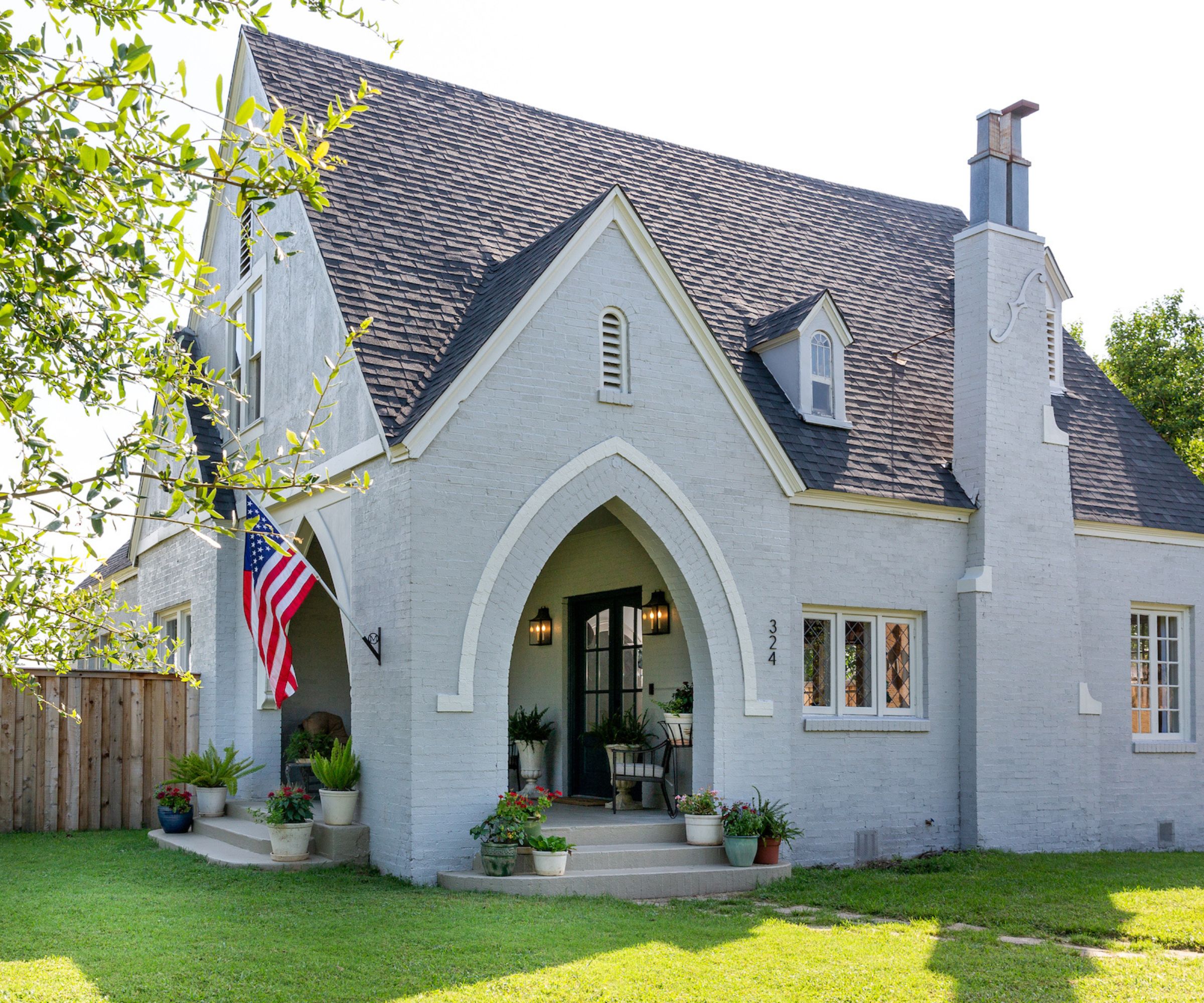 Tudor revival style house with gray painted exterior, arched doorway, grassy lawn