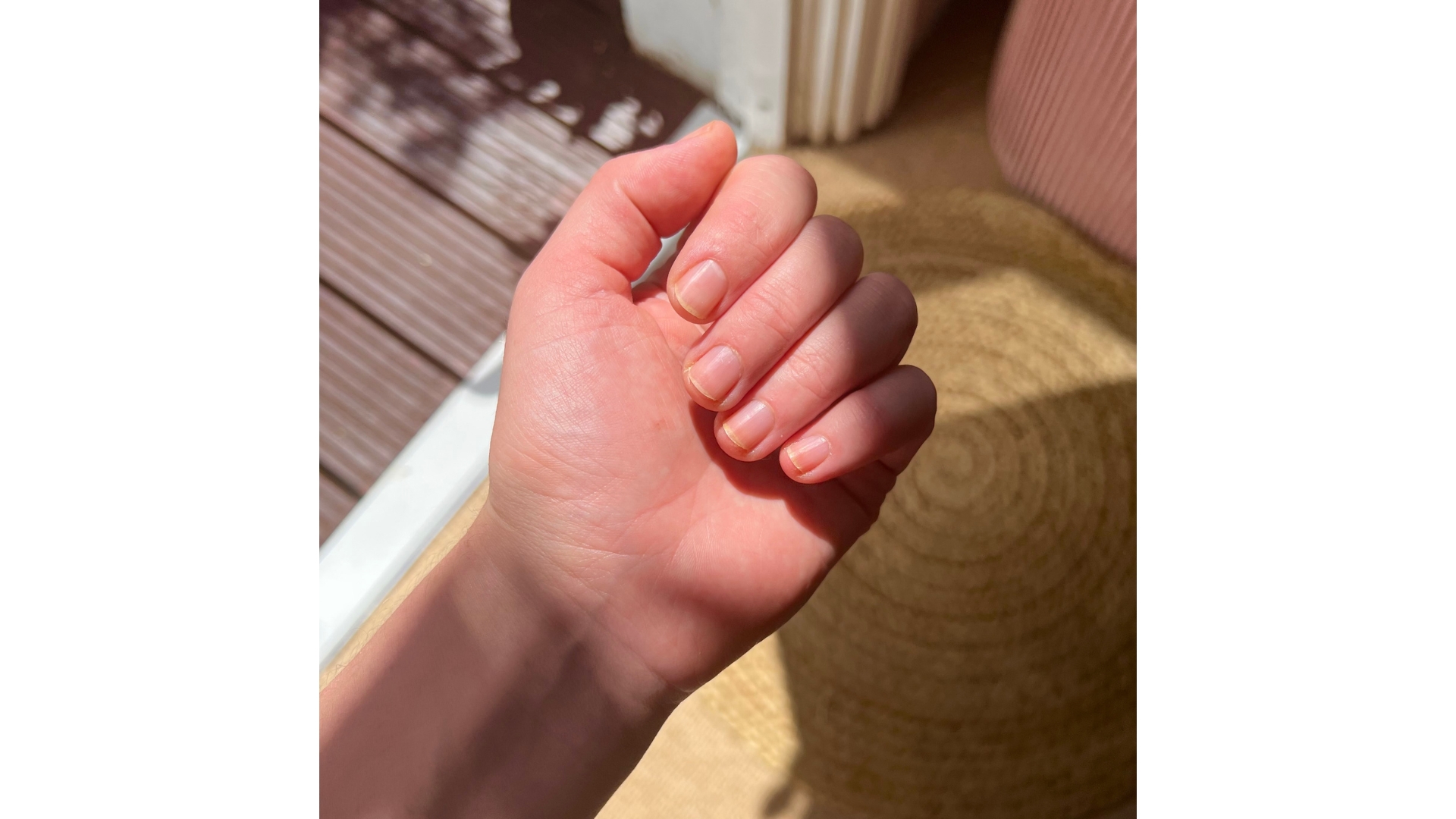 A picture of Digital Beauty Editor, Fiona McKim's hand and natural nails, in front of wooden flooring and carpet background