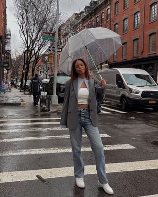 @_sierramayhew wearing grey blazer, white top, blue jeans, and white flats holding and umbrella