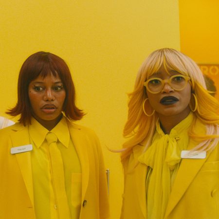Three women (Naomi Ackie as Sade, Taylour Paige as Mariah, Keke Palmer as Corvette) look concerned while wearing all-yellow outfits and standing in a yellow store, in 'I Love Boosters'