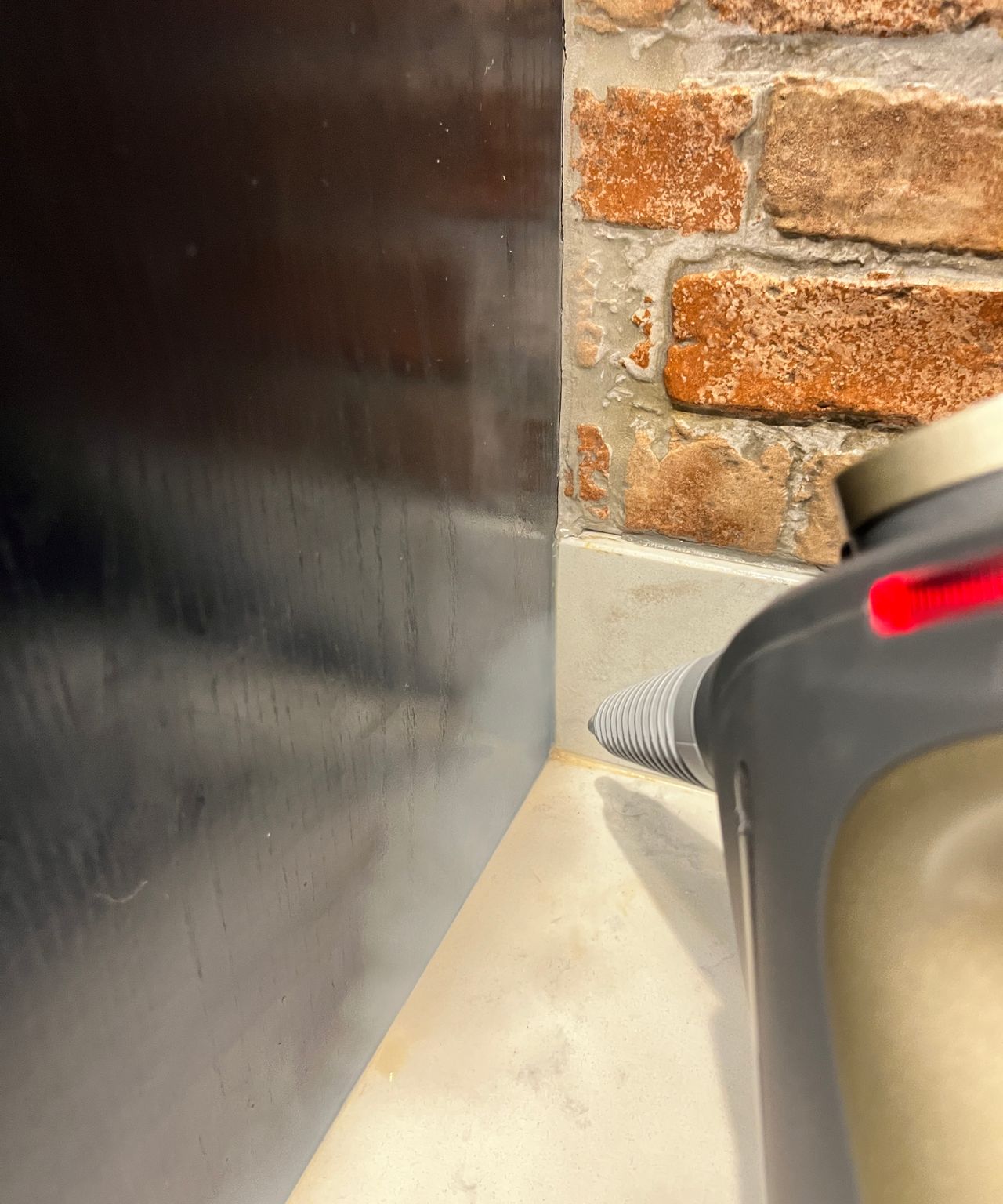 steam cleaner being used in corner of kitchen worktop on tiled upstand with navy cupboard on one side and brick tiles on wall
