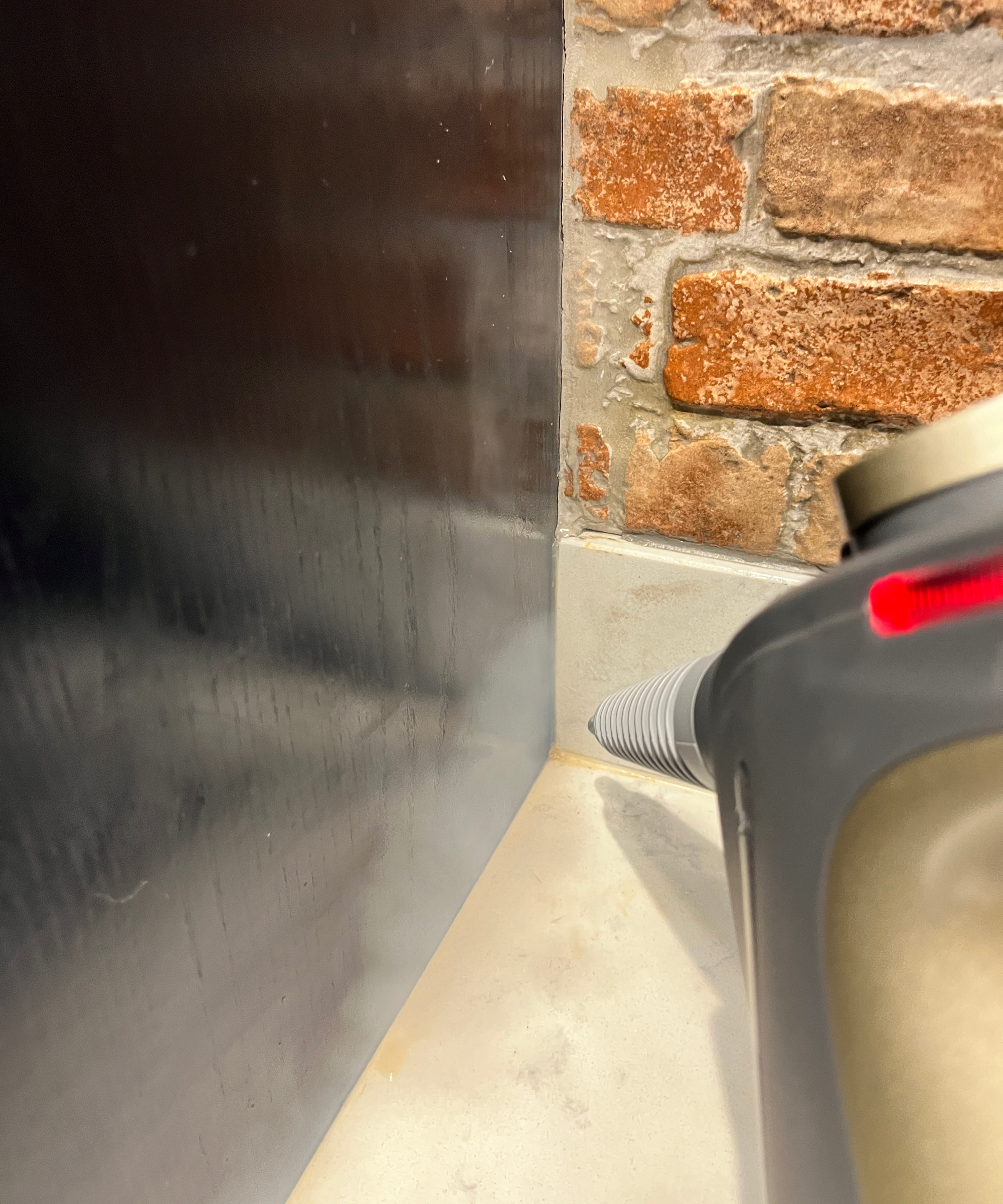 steam cleaner being used in corner of kitchen worktop on tiled upstand with navy cupboard on one side and brick tiles on wall