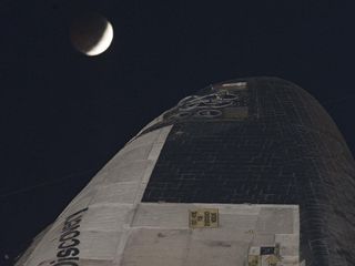 Space shuttle Discovery waits to roll back from Launch Pad 39A to the Vehicle Assembly Building (VAB) at NASA's Kennedy Space Center in Florida in the early morning hours of Dec 21, 2010, with the beginning of the total lunar eclipse clearly in view.