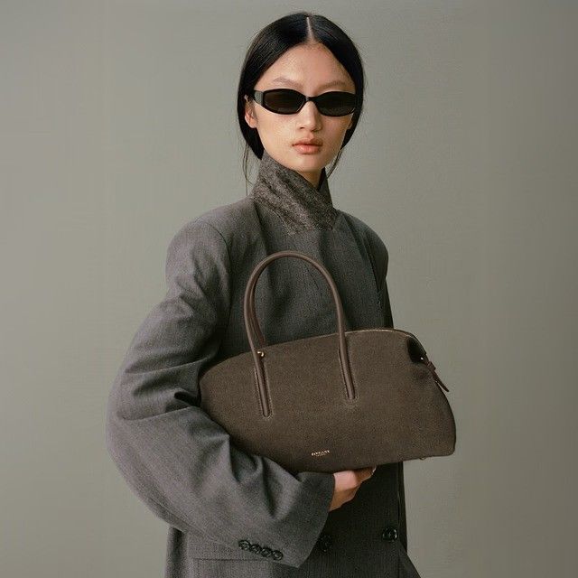 Model wears black sunglasses, grey blazer, green suede midi bag