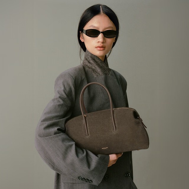 Model wears black sunglasses, grey blazer, green suede midi bag