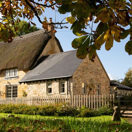 exterior of a cotswolds thatched cottage with a stone built side extension