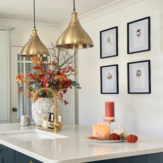 brass lights over an island with sink in white kitchen