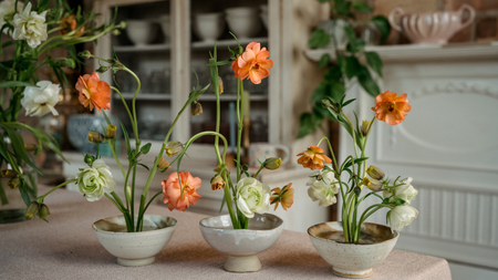 Floral design with peach and cream butterfly ranunculus in three ceramic bowls