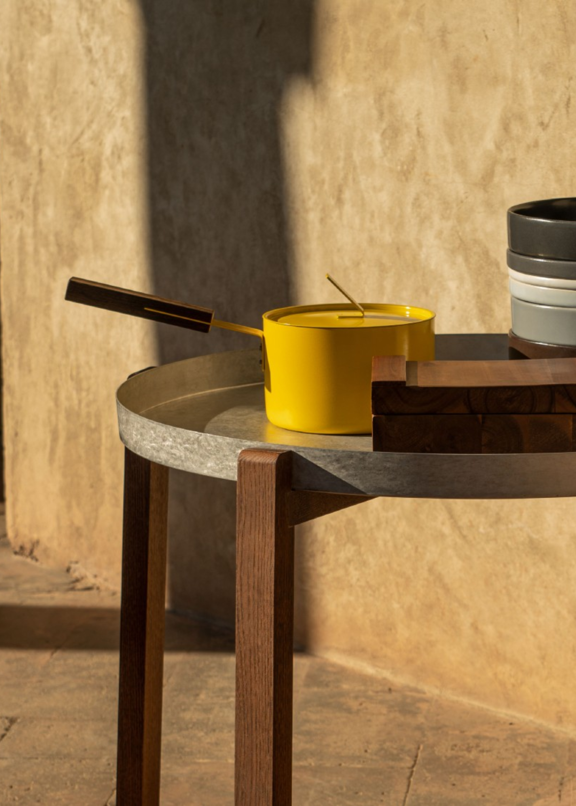 A yellow pot with a lid and a wood handle on a side table outdoors