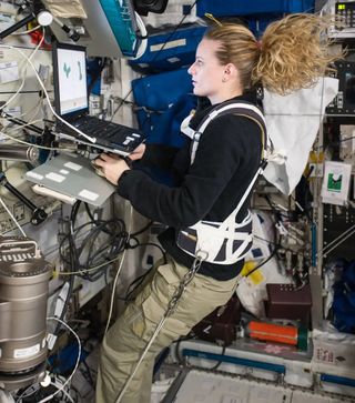 an astronaut looking at a computer screen while floating in a space station module